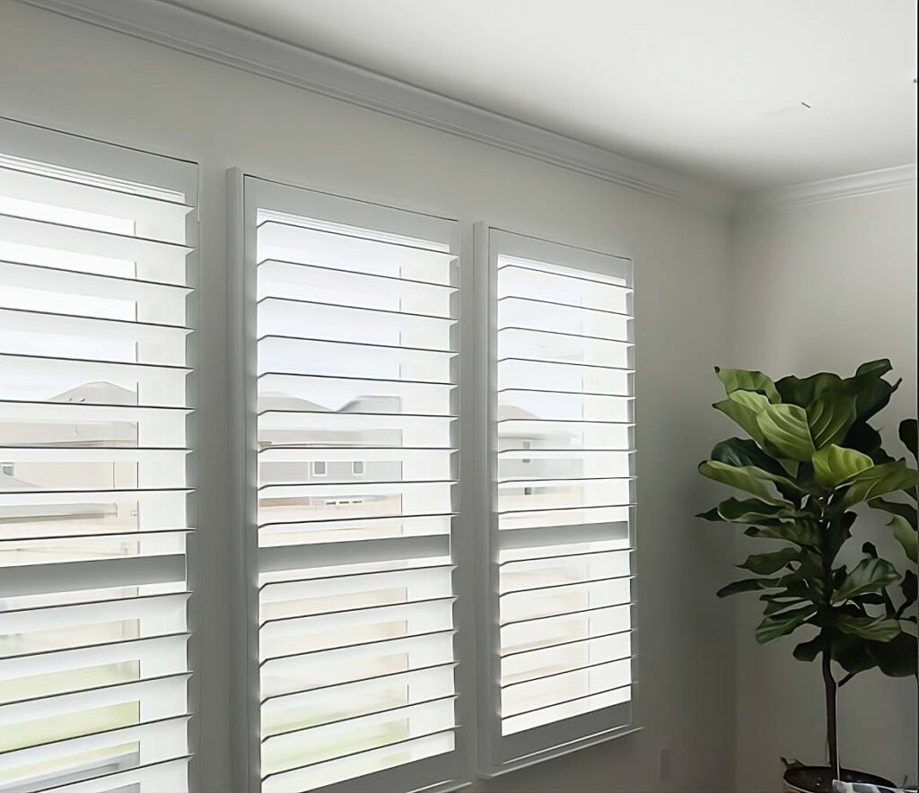 Texas Made Shutters on three windows in a residential living room with a house plant nearby at Kerrville Window Fashionsnear Kerrville, TX