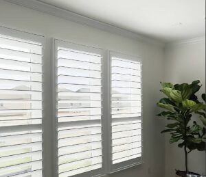 Texas Made Shutters on three windows in a residential living room with a house plant nearby at Kerrville Window Fashionsnear Kerrville, TX