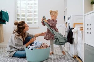 Child helping their mother in the laundry room with window blinds on the window behind them near Kerrville, TX