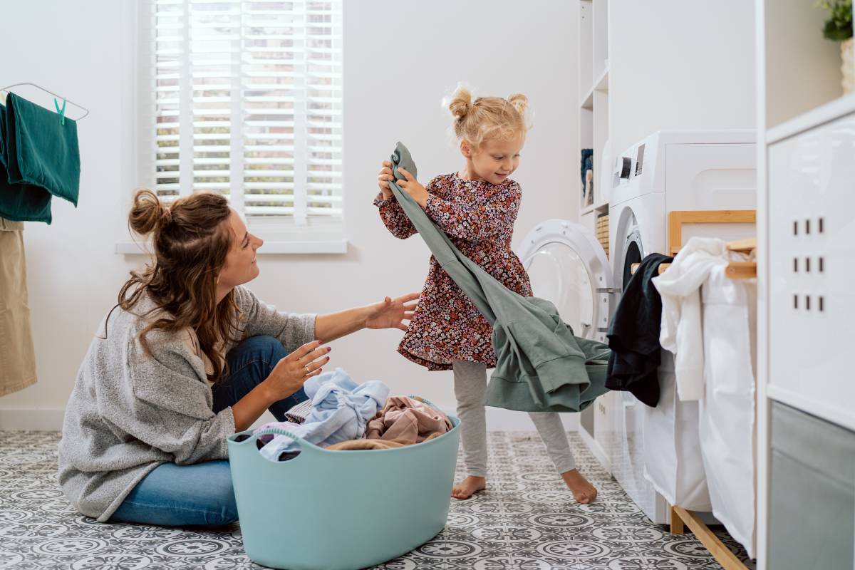 Child helping their mother in the laundry room with window blinds on the window behind them near Kerrville, TX