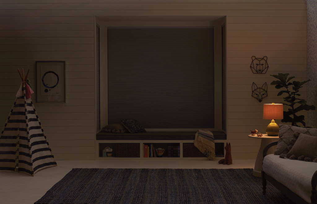 A cozy nursery room with cordless cellular shades with room-darkening enhancements on the window